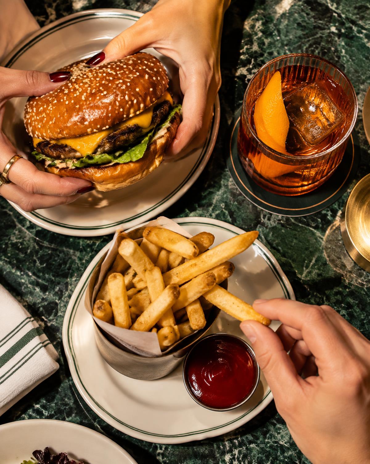 Manos compartiendo una hamburguesa y papas fritas en un restaurante